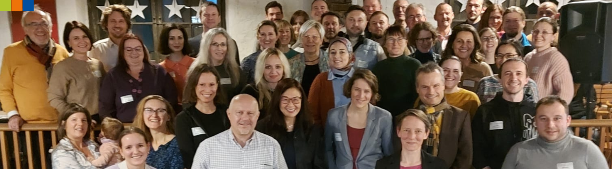 Gruppenfoto der Teilnehmer*innen des 17. Mentoring-Durchgangs der Mentoring-Partnerschaft Augsburg, aufgenommen im Café Tür an Tür. Menschen aus 12 Ländern und verschiedenen Berufen feiern gemeinsam den Abschluss.